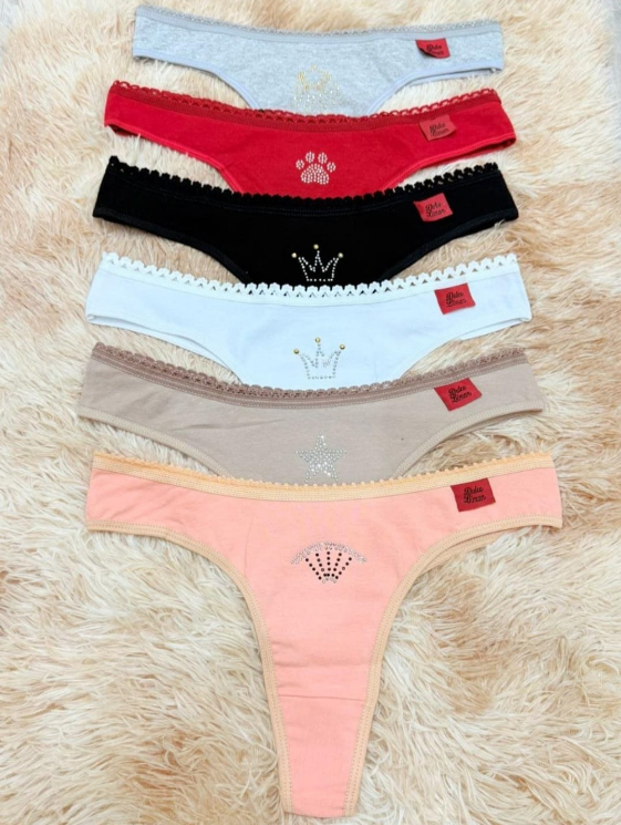 Cinco coloridas piezas de ropa interior tipo tanga exhibidas sobre una superficie esponjosa de color crema; varios colores y diseños de coronas o patas.