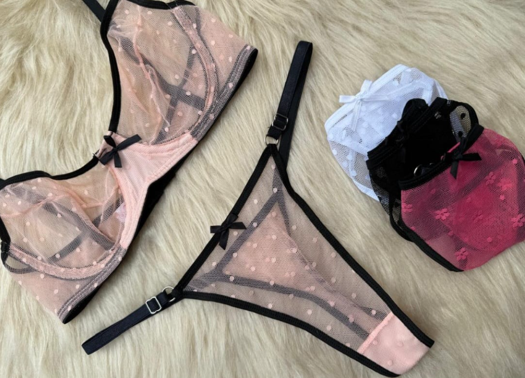 Conjunto de lencería rosa con ribete negro y un montón de tangas a juego sobre una superficie esponjosa de color claro.