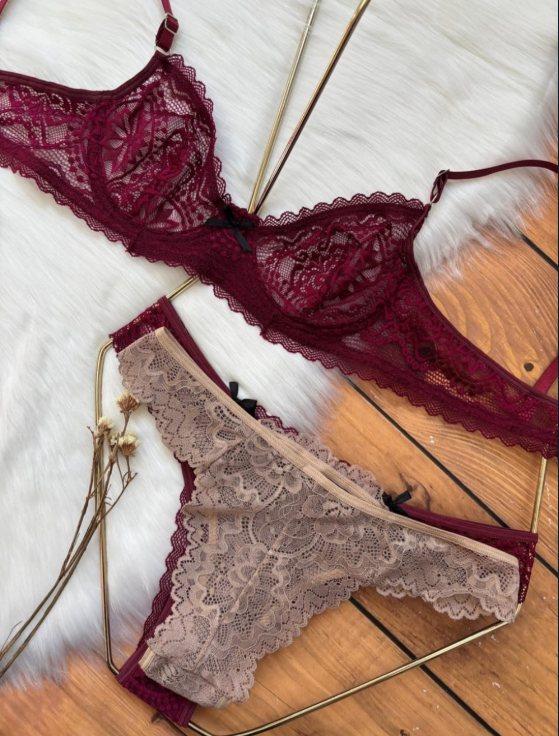 Conjunto de lencería de encaje burdeos: sujetador y tanga con pequeños lazos negros, sobre una superficie blanca esponjosa.