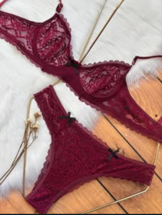 Conjunto de lencería de encaje burdeos: sujetador y tanga con pequeños lazos negros, sobre una superficie blanca esponjosa.