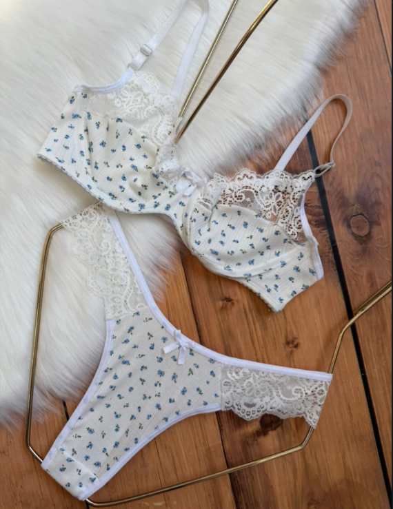 Conjunto de lencería con estampado floral sobre una superficie de piel blanca y madera. Incluye sujetador, tanga y dos calzoncillos.