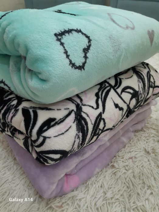 Tres mantas dobladas: verde azulado con corazones, floral en blanco y negro, y lavanda.