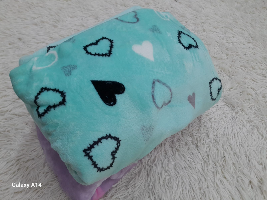 Tres mantas dobladas: verde azulado con corazones, floral en blanco y negro, y lavanda.