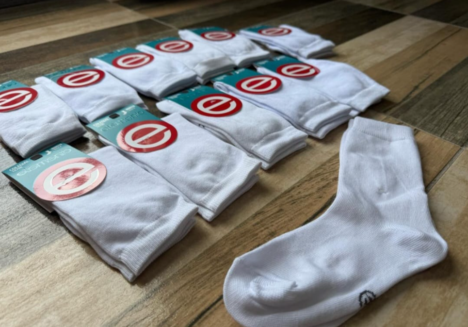 Calcetines blancos, algunos con etiquetas, expuestos sobre una superficie con dibujos de madera.