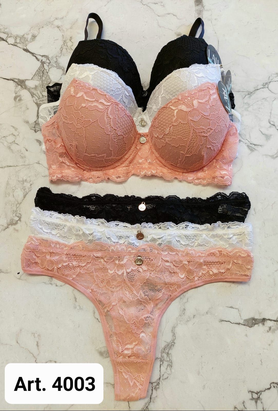 Conjunto de lencería de encaje: sujetadores y tangas en negro, blanco y melocotón sobre una superficie de mármol. Etiqueta 
