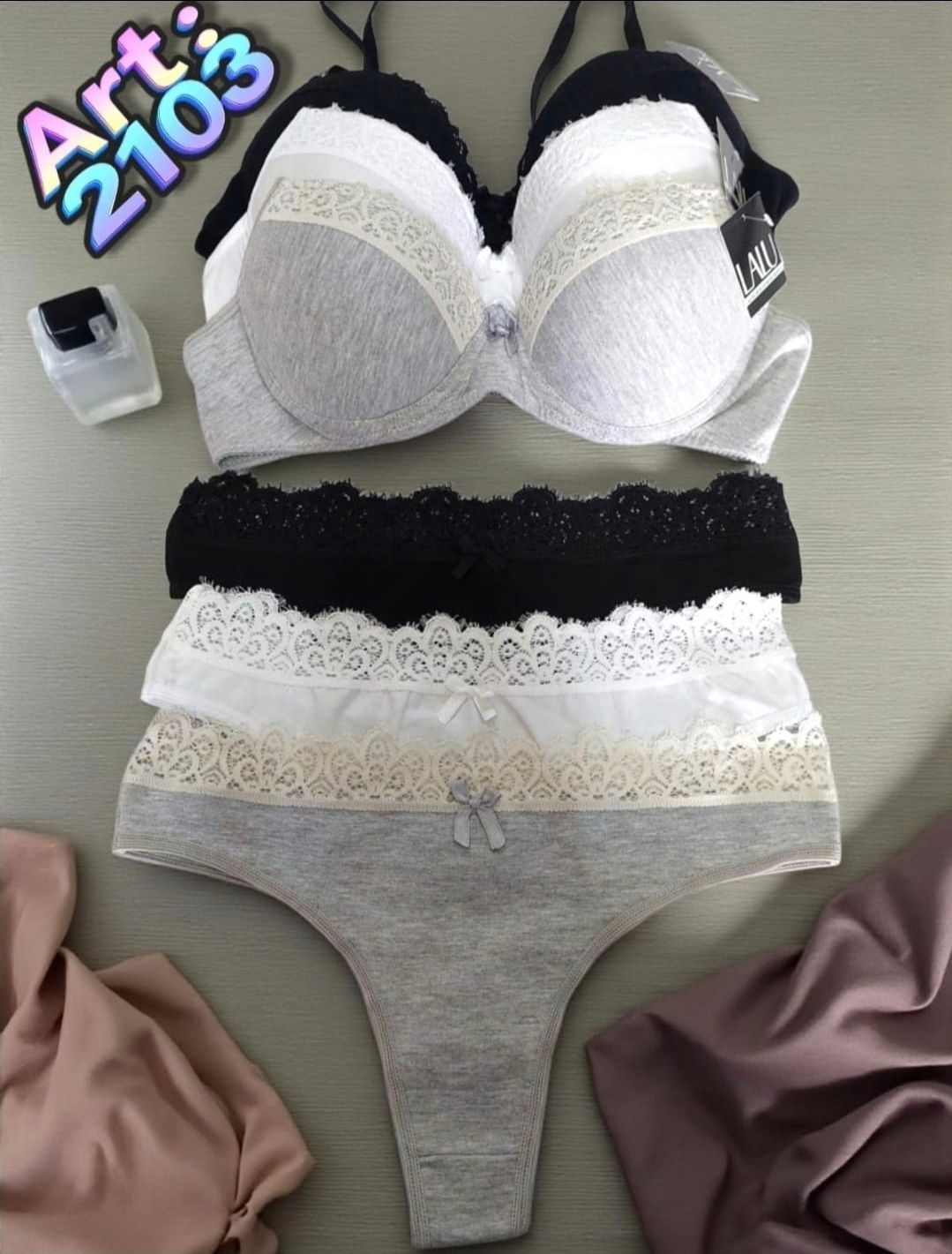 Conjunto de sujetador y ropa interior en color blanco, gris y negro con ribete de encaje, sobre superficie gris.