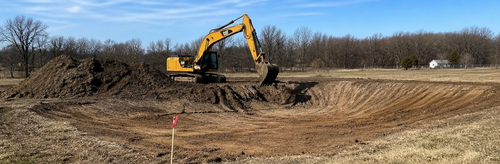 Yellow excavator working on a dirt lot under a clear sky
