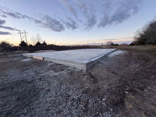 Deep trench cut through dry earth beside brush, with trees lining the horizon under a blue sky