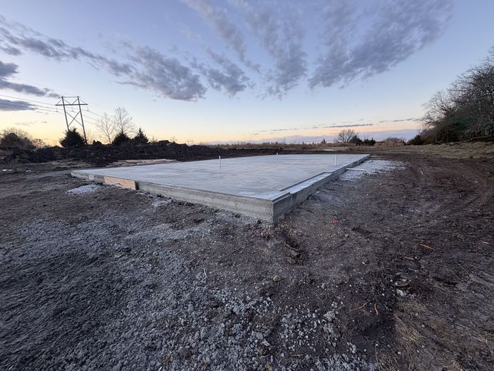 Deep trench cut through dry earth beside brush, with trees lining the horizon under a blue sky
