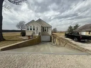 Small house with driveway and garage on a rural roadside under a cloudy sky