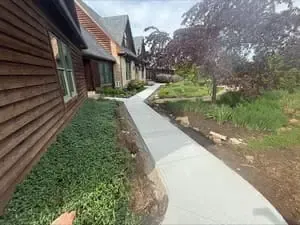 Curved concrete walkway beside rustic wooden houses and greenery in a garden setting