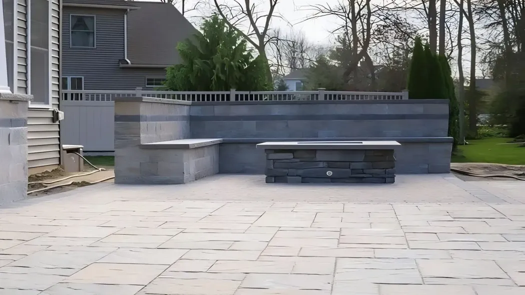 Modern stone patio with built-in bench seating in a backyard beside a house