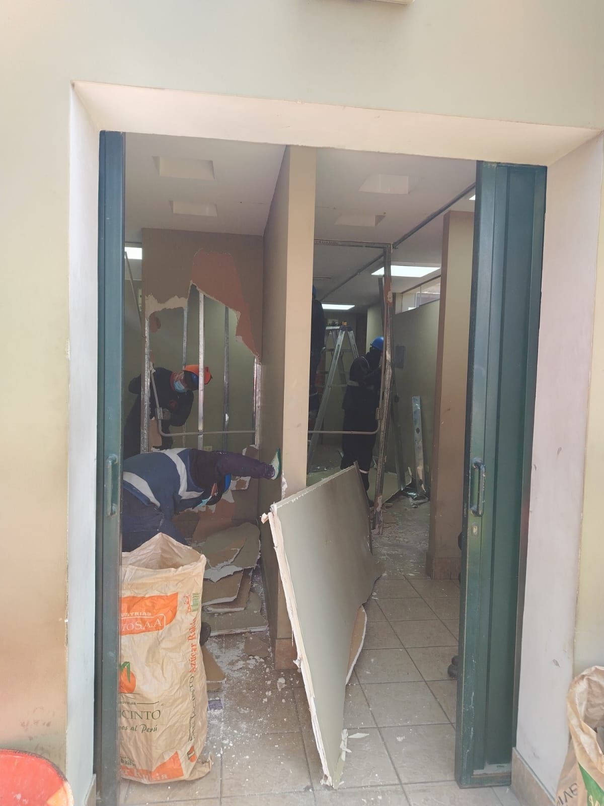 Puerta de acceso a pasillo con escombros de construcción, dos figuras en ropa de trabajo, interior.