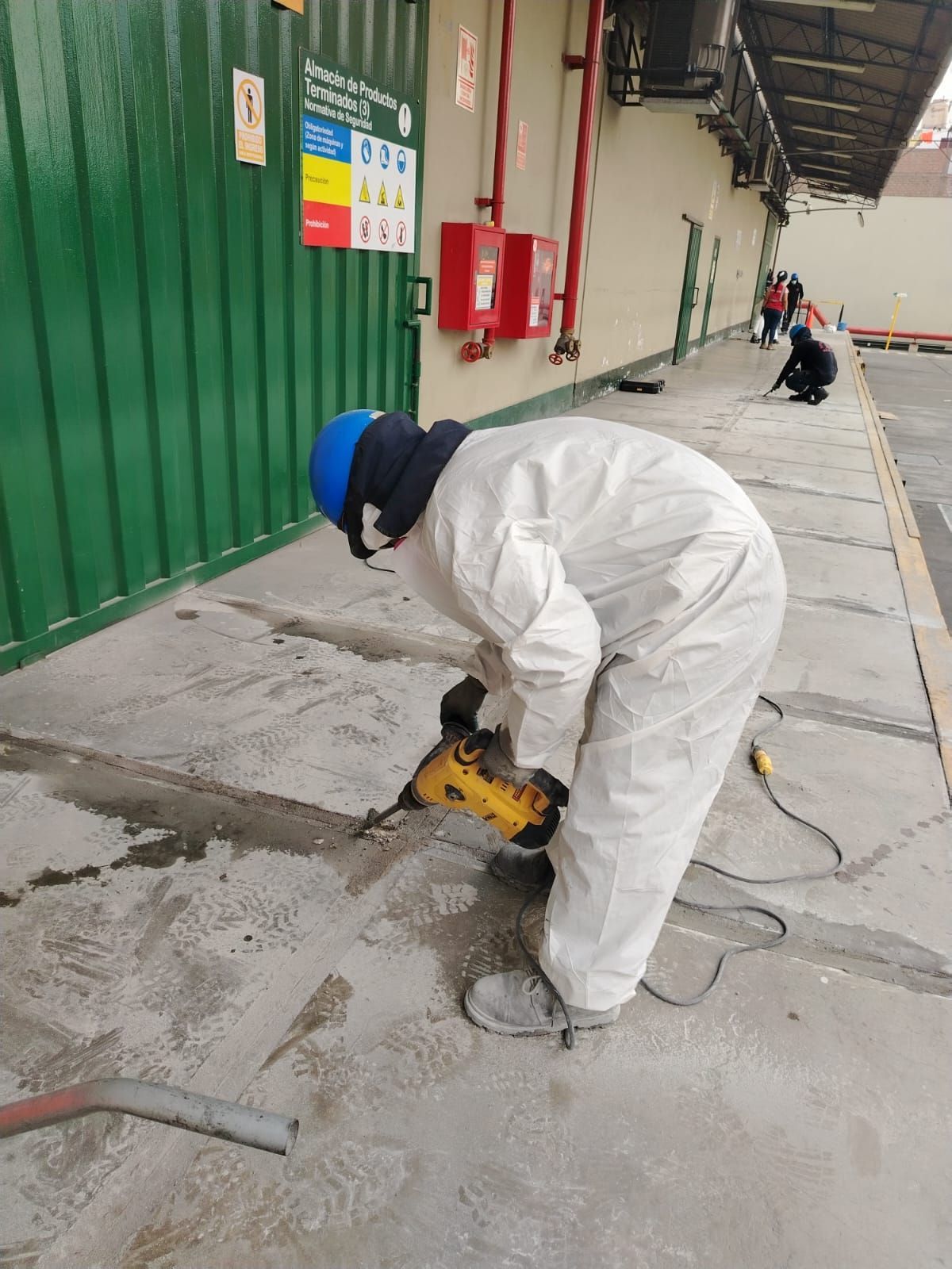 Persona con traje de protección blanco utilizando un martillo neumático sobre hormigón en el exterior de un edificio.