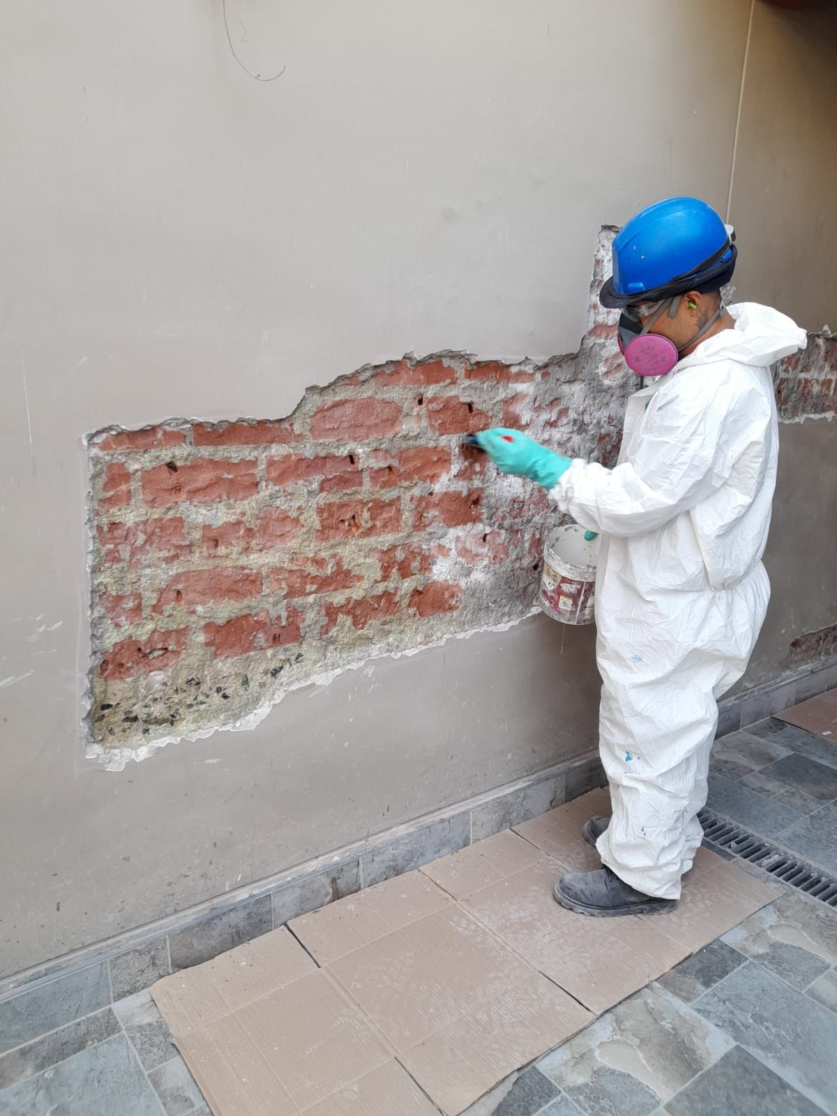 Persona con traje de protección rociando una pared de ladrillos con una sección de yeso dañada.