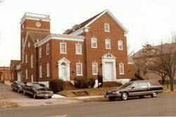 Red brick building with hearse and cars parked out front.
