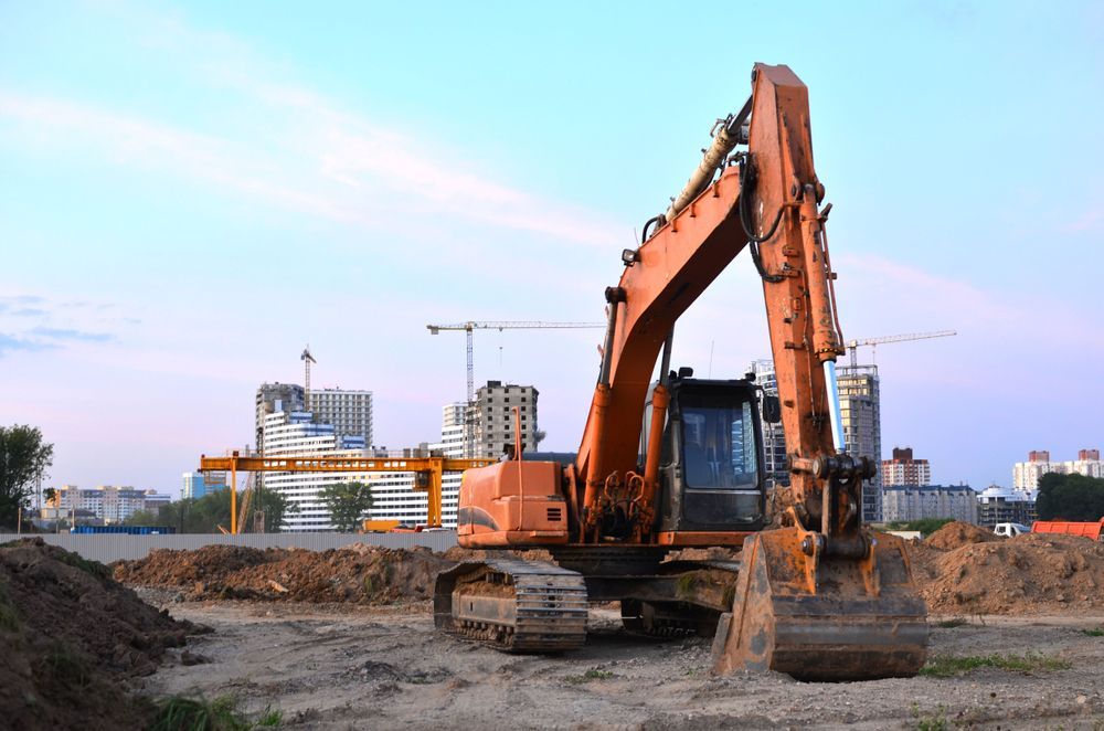 Orange Excavator on a Construction Site With Buildings — Jim Anderson Earthmoving Pty Ltd In Gloucester, NSW