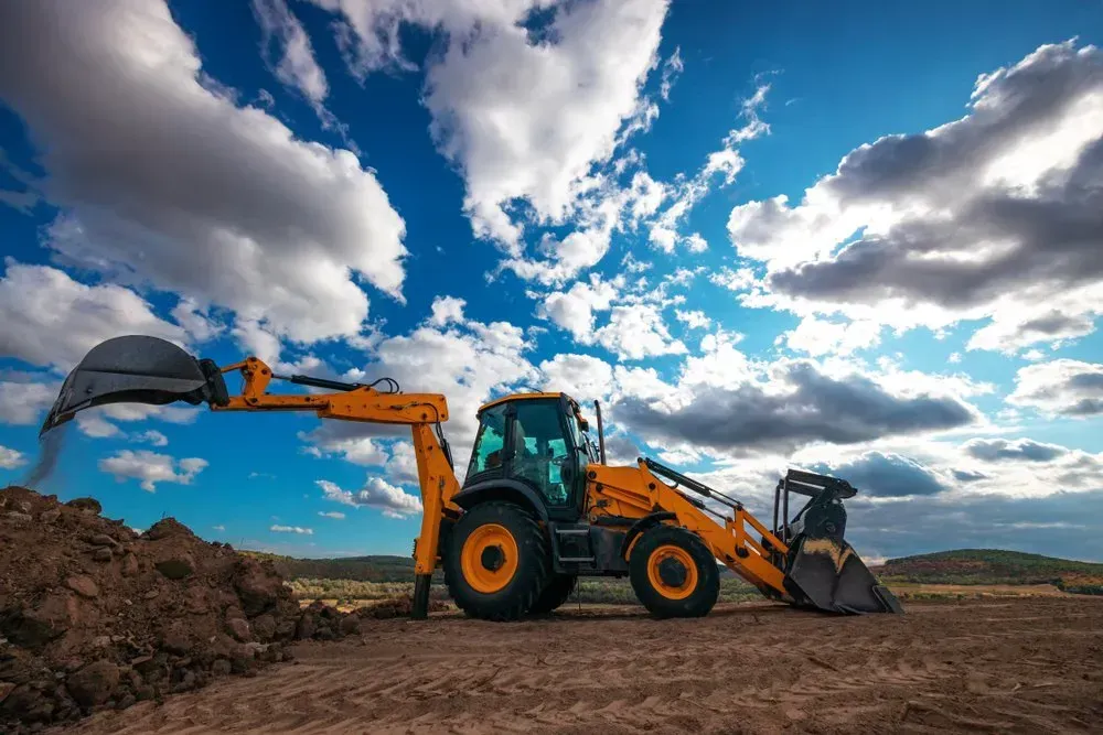 Yellow Backhoe on Brown Dirt Under Blue Sky with Clouds — Jim Anderson Earthmoving Pty Ltd in Coopernook, NSW