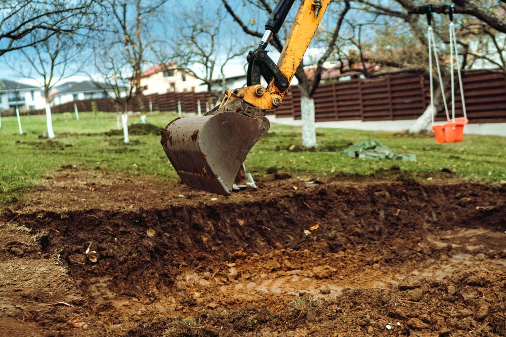 A Yellow Excavator Digging a Trench in a Grassy Backyard — Jim Anderson Earthmoving Pty Ltd In Forster, NSW