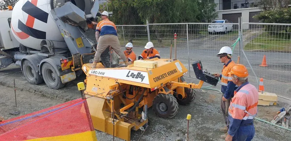 Construction crew working with a cement mixer and yellow curbing machine on a paved road surface