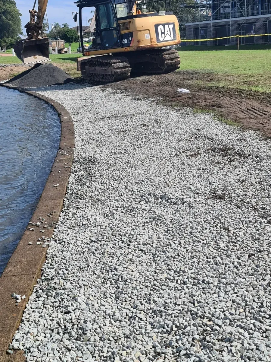 An Excavator Spreads Gravel Along the Edge of a Body of Water — Jim Anderson Earthmoving Pty Ltd In Coopernook, NSW