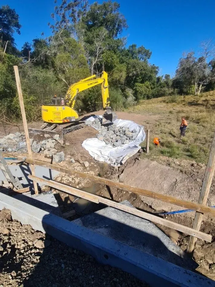 Yellow Excavator Placing Large Rocks in A Construction Site — Jim Anderson Earthmoving Pty Ltd in Coopernook, NSW