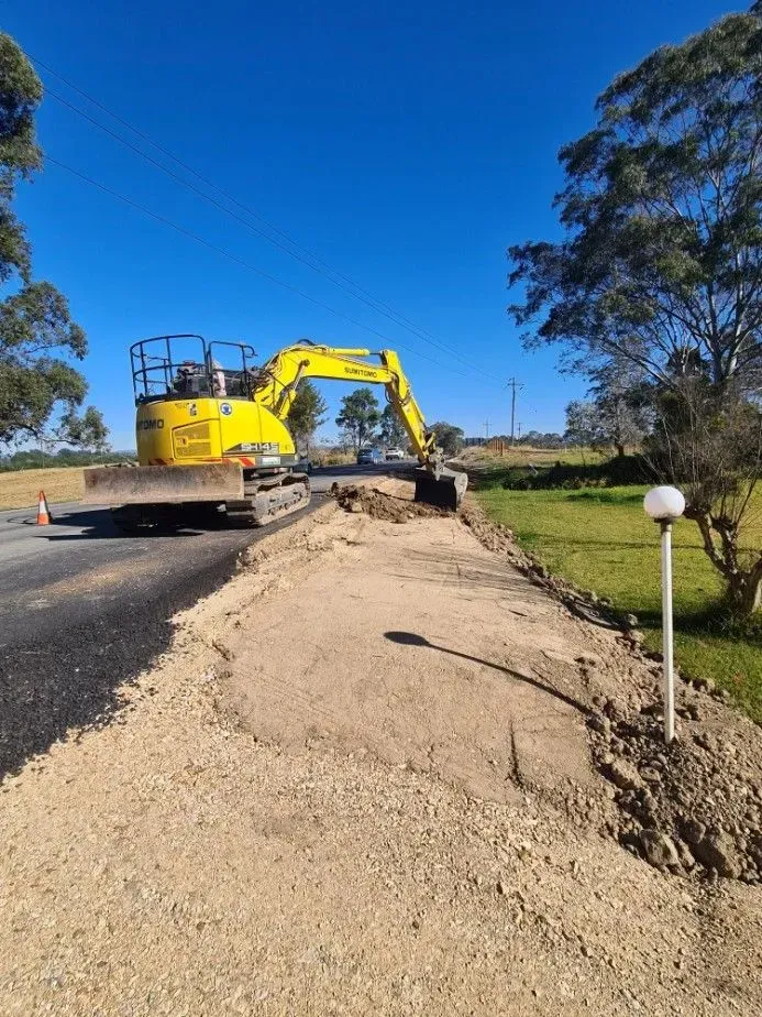 Yellow Excavator Removing Asphalt from A Road — Jim Anderson Earthmoving Pty Ltd in Coopernook, NSW