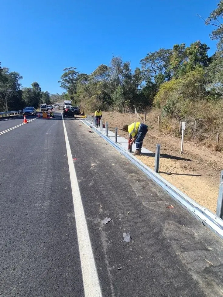Road Workers Installing a Guardrail on a Highway Shoulder Under a Blue Sky — Jim Anderson Earthmoving Pty Ltd In Forster, NSW