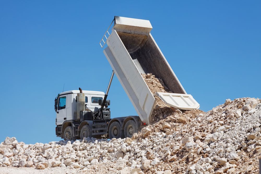 White Dump Truck Unloading Rocks Against a Clear Blue Sky — Jim Anderson Earthmoving Pty Ltd In Forster, NSW