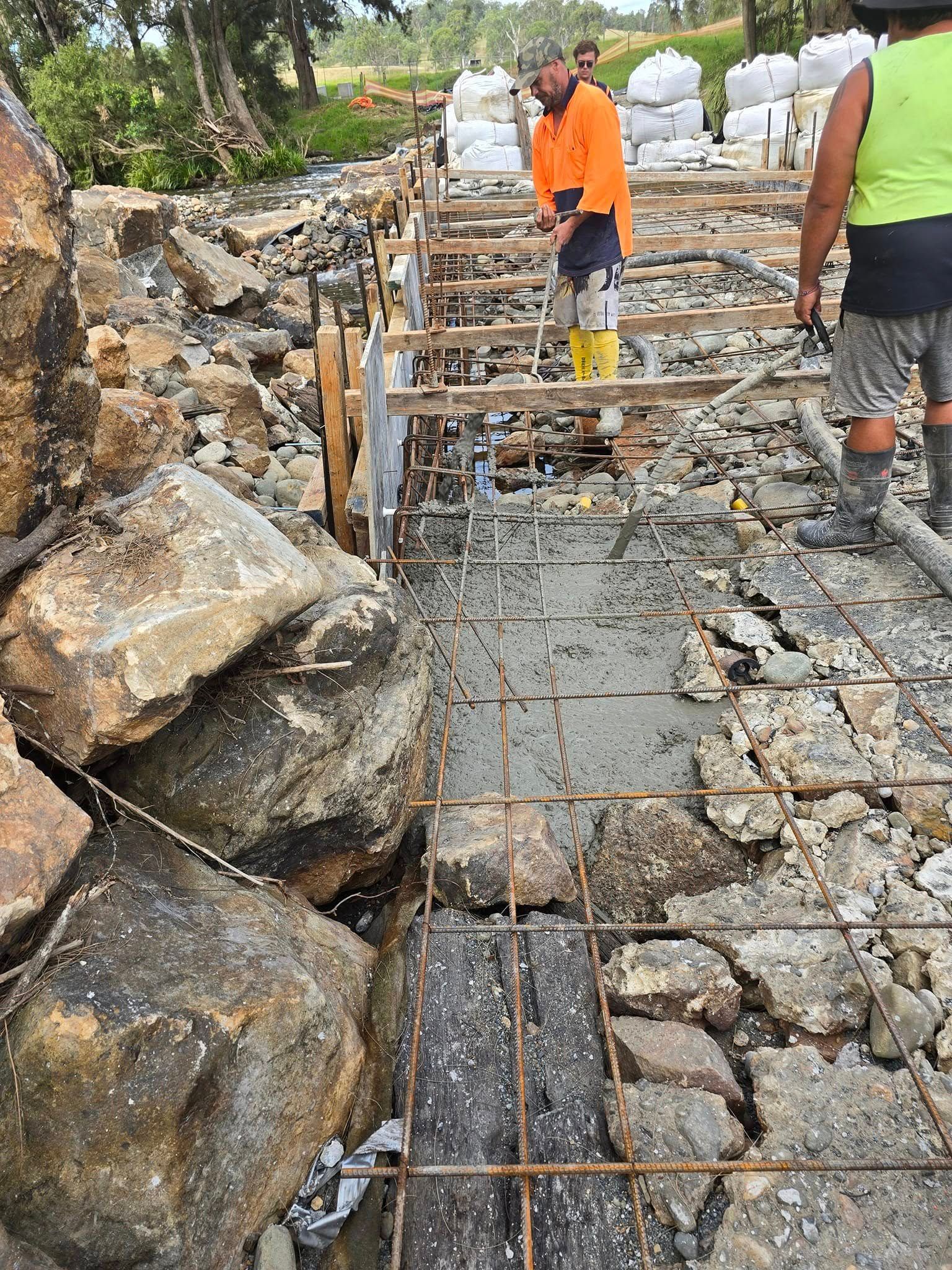 Construction workers pouring concrete between rocks; one uses a tool — Jim Anderson Earthmoving Pty Ltd In Coopernook, NSW