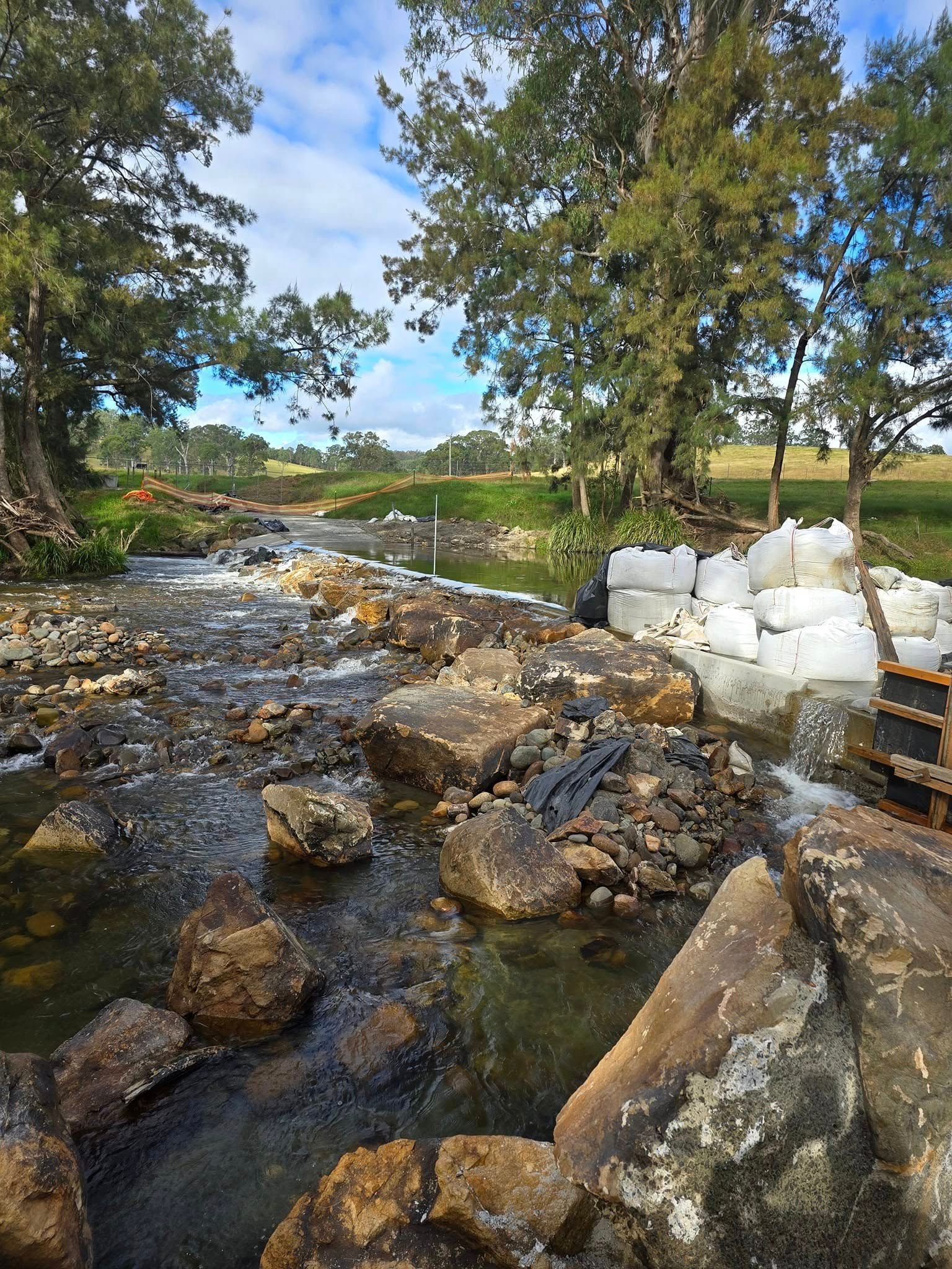 Rocky creek flowing through a green landscape with trees and a cloudy sky — Jim Anderson Earthmoving Pty Ltd In Coopernook, NSW