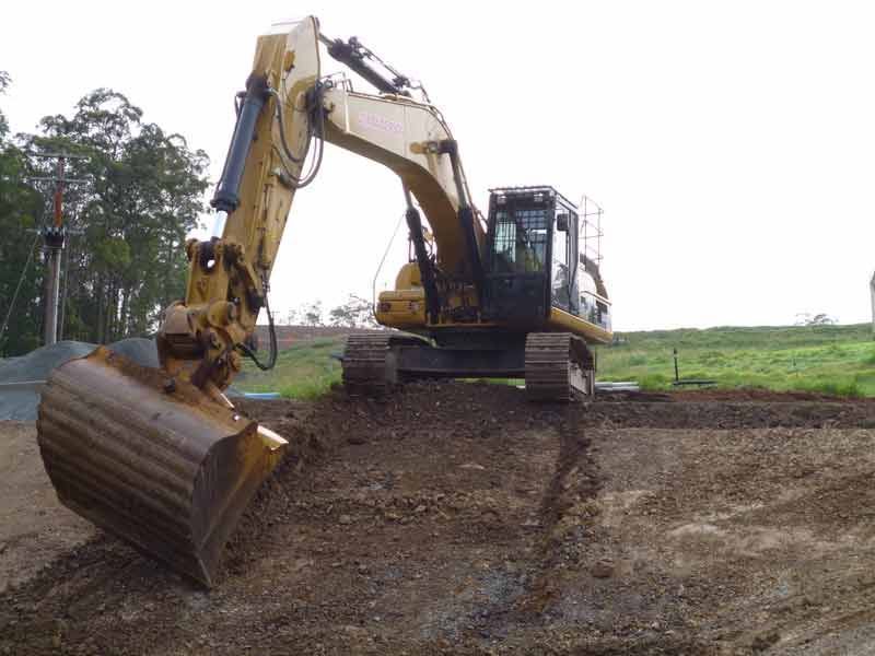 Yellow Excavator Digging Into a Dirt — Jim Anderson Earthmoving Pty Ltd In Wingham, NSW
