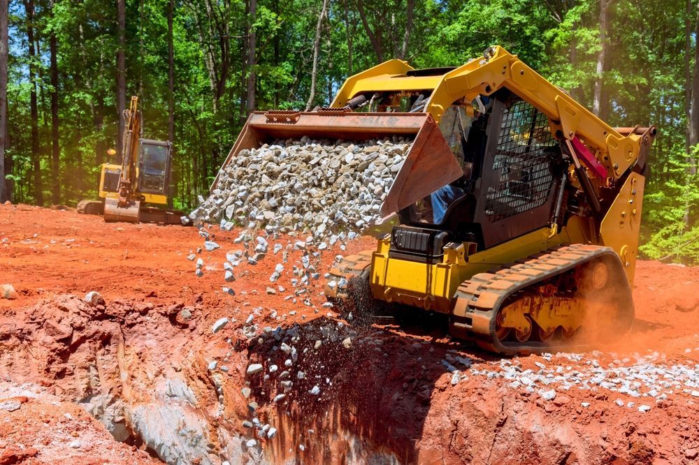 Yellow Skid Steer Dumping Gravel Into a Trench on a Construction Site — Jim Anderson Earthmoving Pty Ltd In Old Bar, NSW