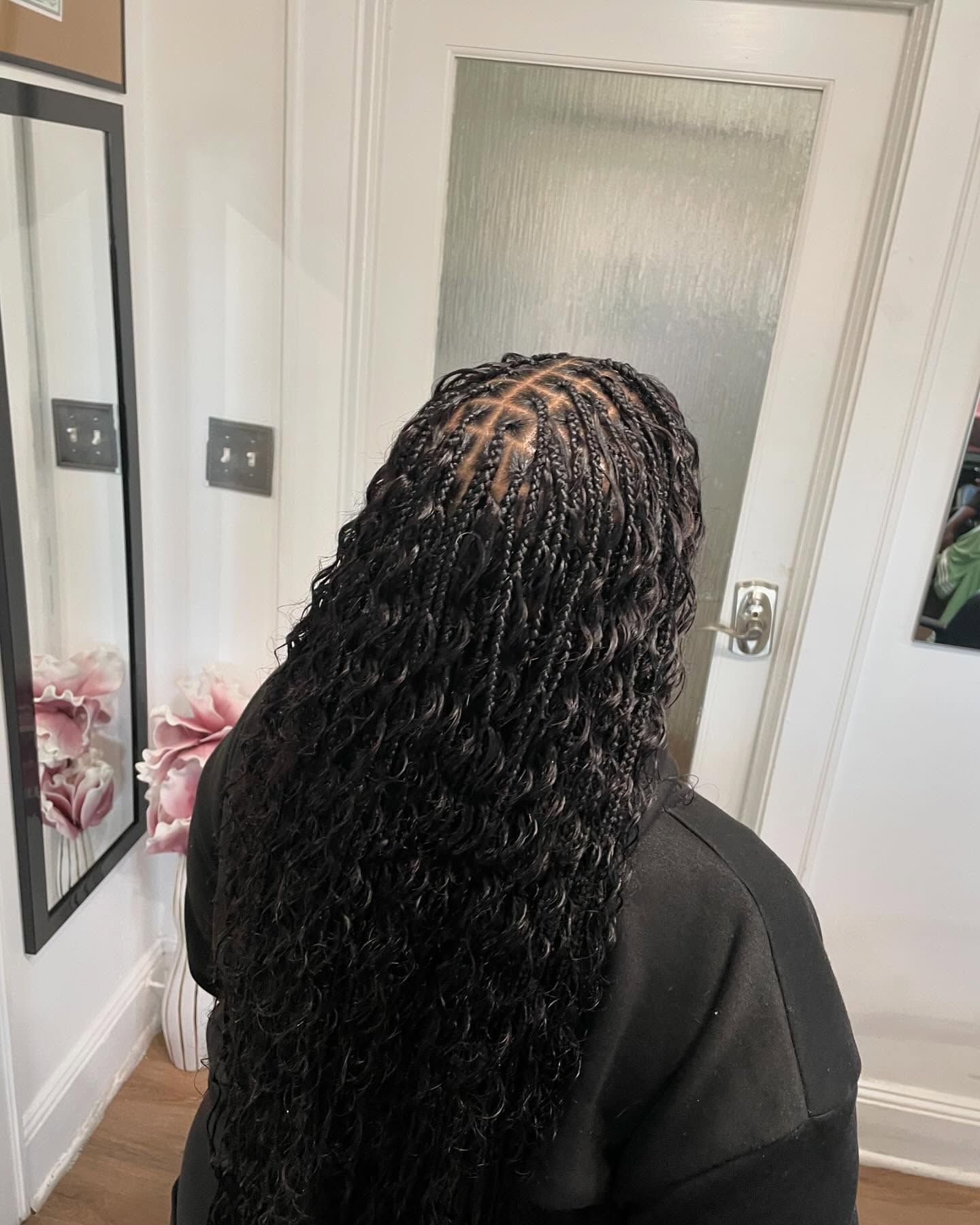 Woman with long, black, curly micro locs hairstyle. Indoors, near a mirror and white door.