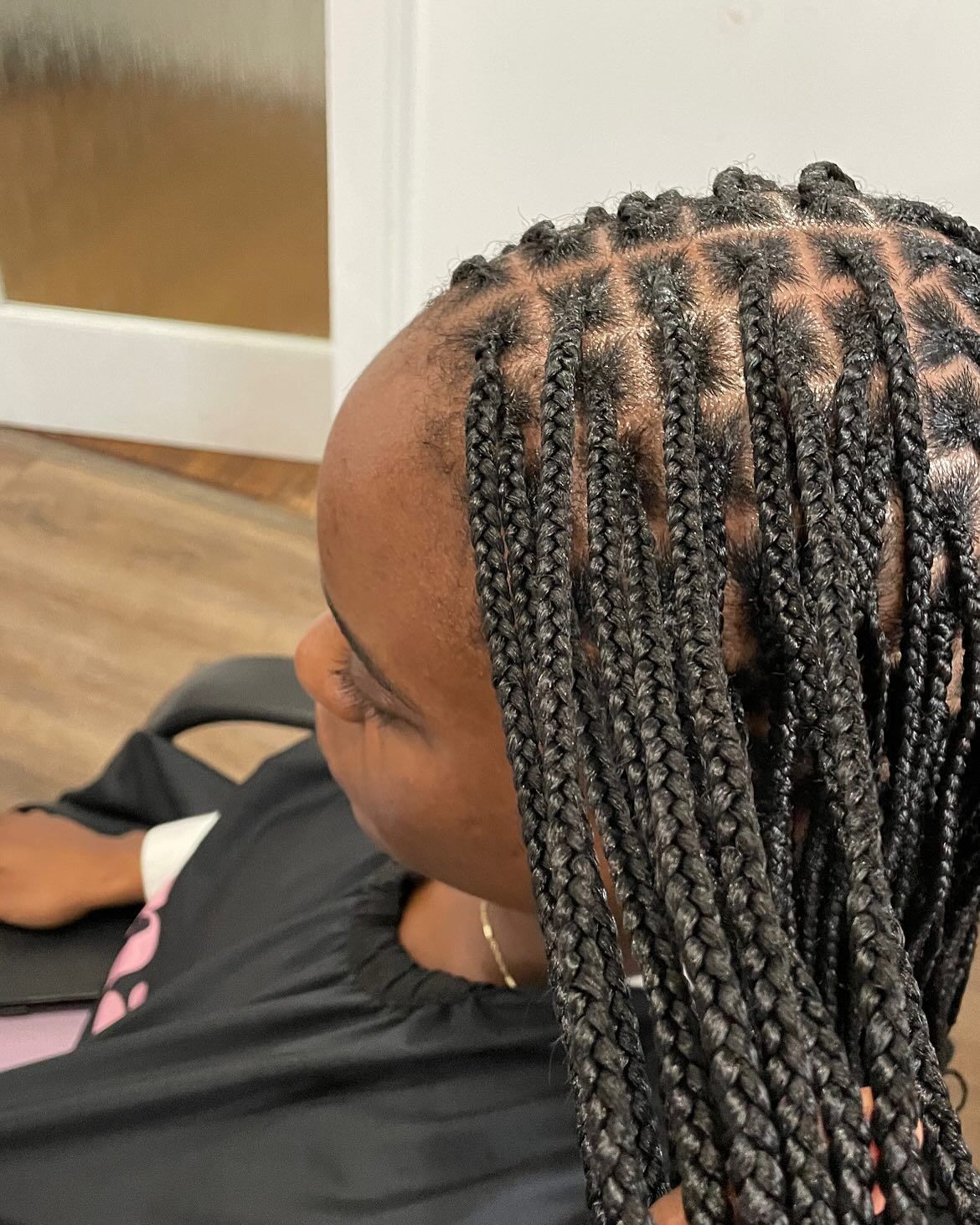 A person with black box braids, sitting in a salon chair.
