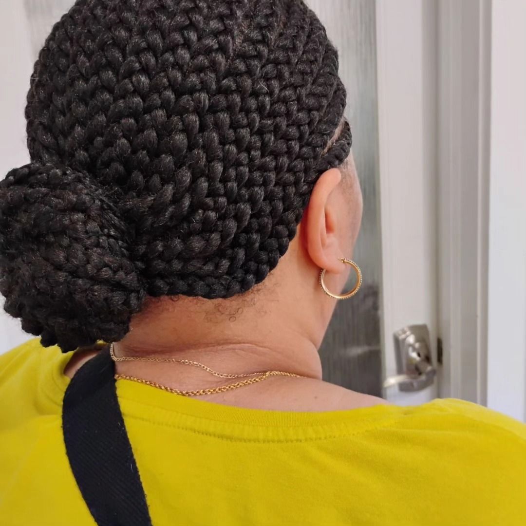 Woman with dark braided hair in a bun, wearing a yellow shirt and gold hoop earrings.