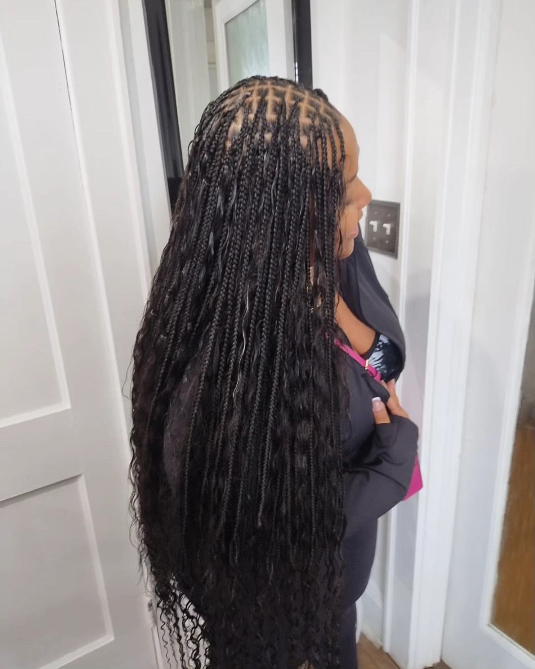Woman with long, black micro braids, standing indoors near a doorway.
