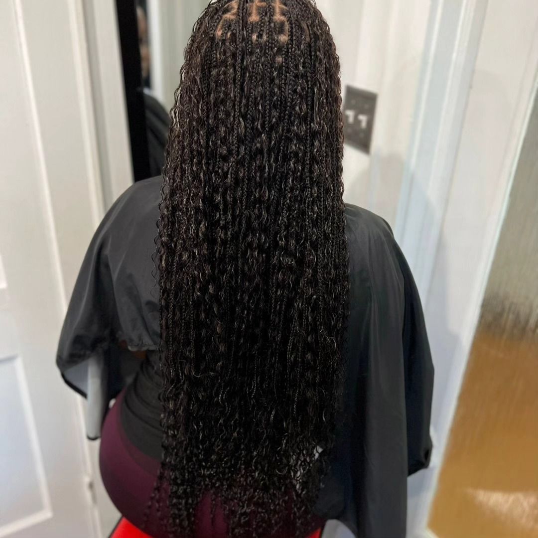Woman with long, dark, micro-braided hair; wearing a black cape; sitting in a brightly lit room.