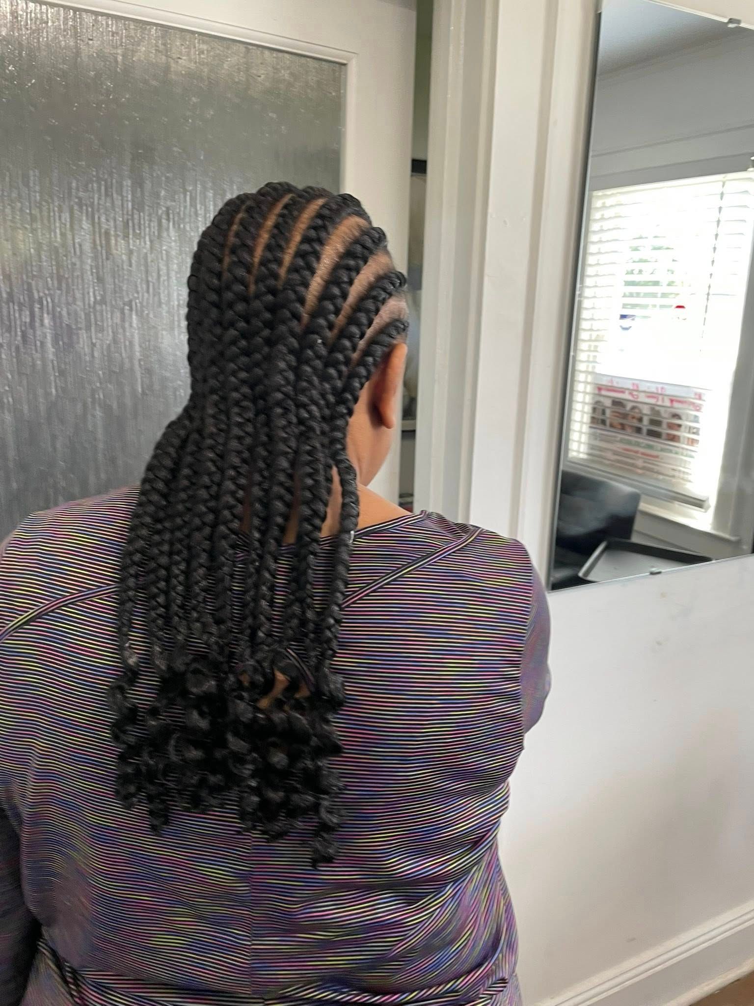 Woman with braided hair, wearing a purple patterned top, standing in front of a mirror.