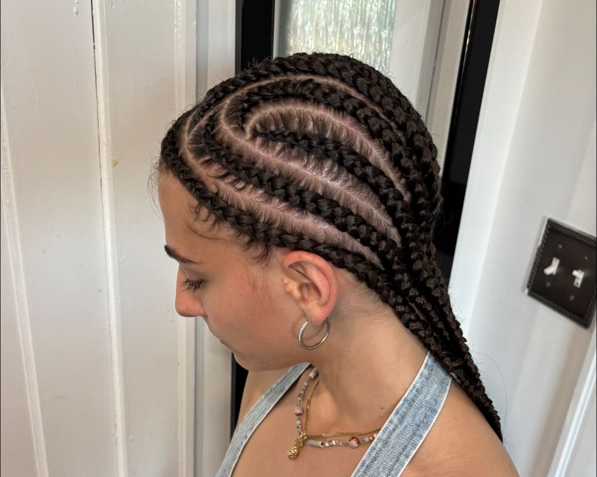 Woman with dark braided hair in a curved cornrow style, wearing a necklace, looking down.