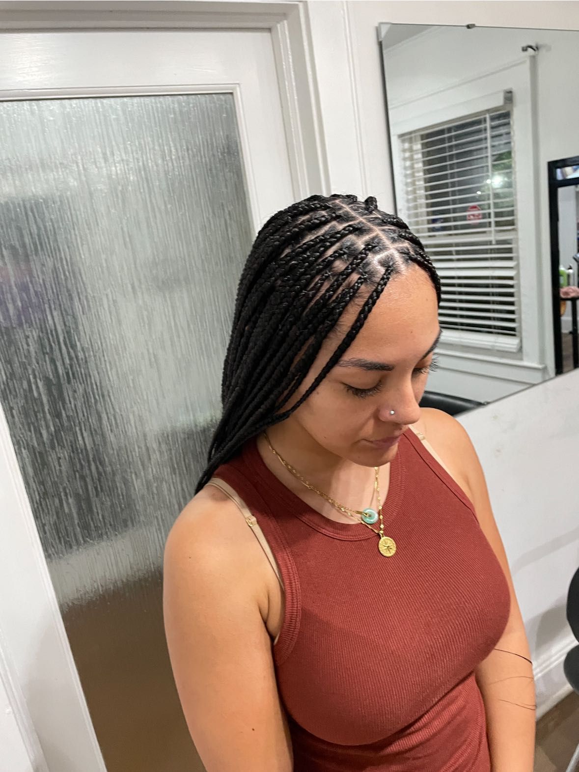 Woman with box braids, wearing a brown tank top, in a salon with a mirror.
