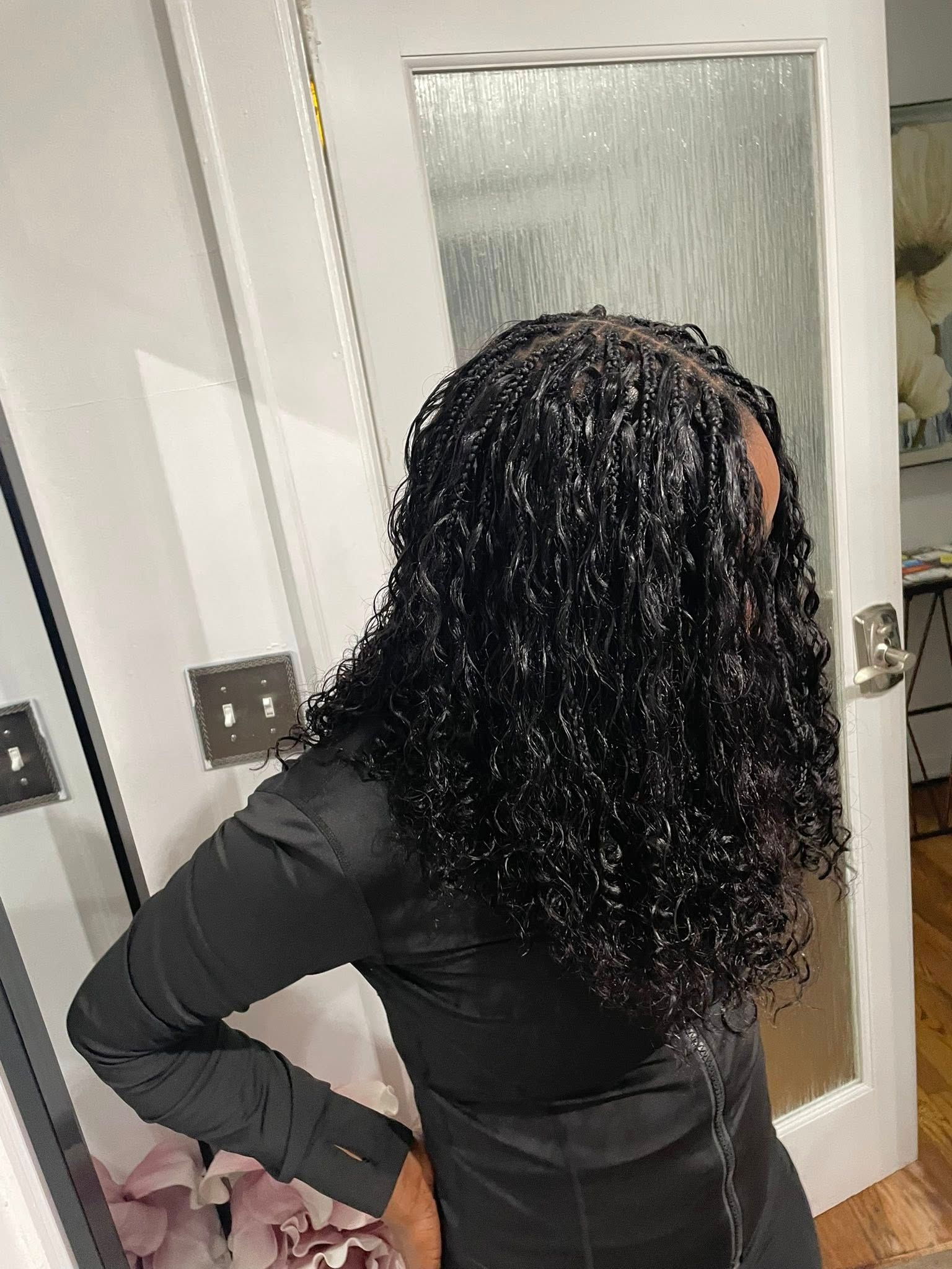 Woman with long, black, wet-looking curly hair wearing a black shirt, standing indoors by a door.