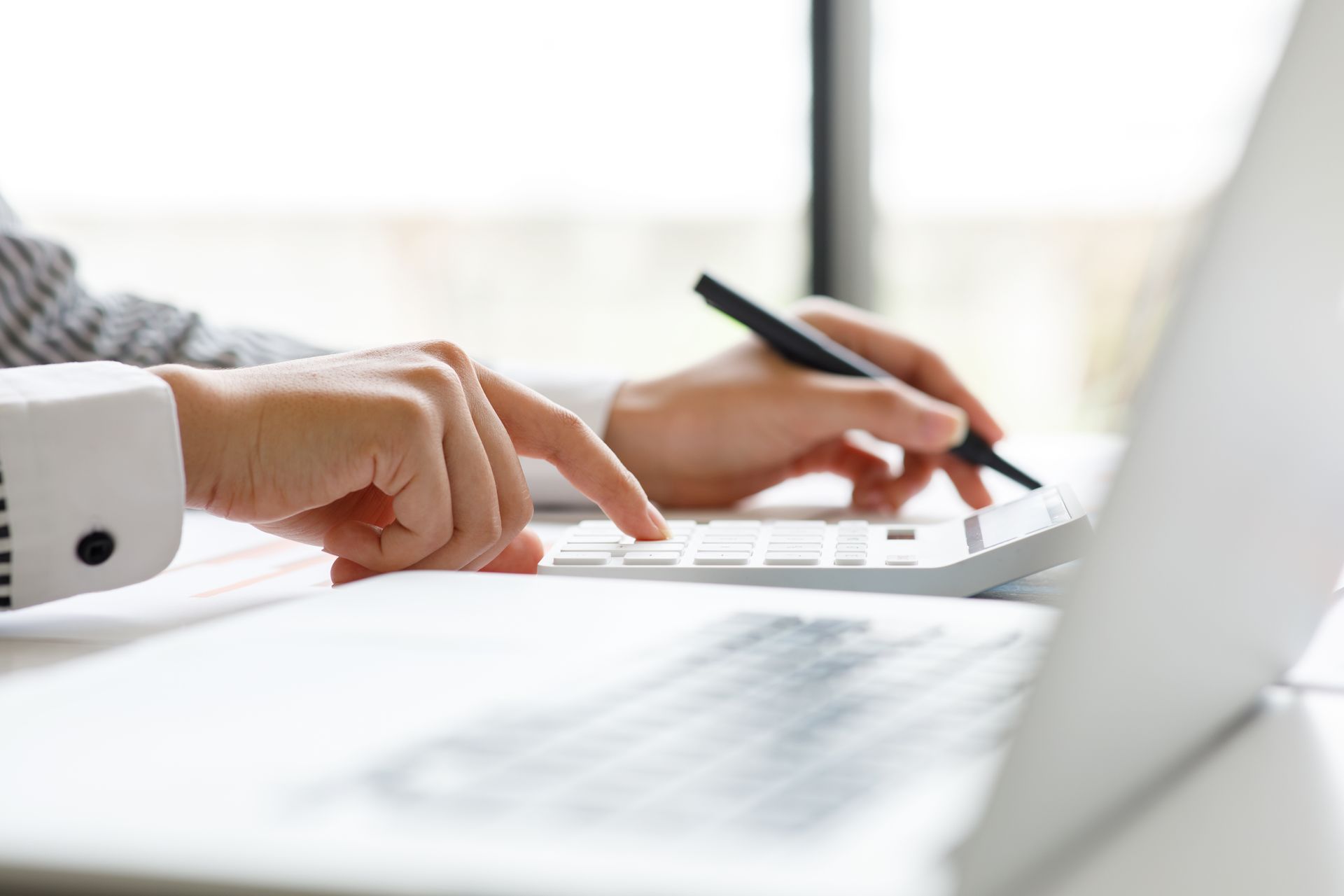 A person is typing on a laptop computer while holding a pen.