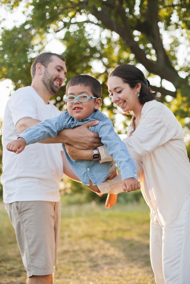 A family lifting a smiling child outdoors in a sunny park.