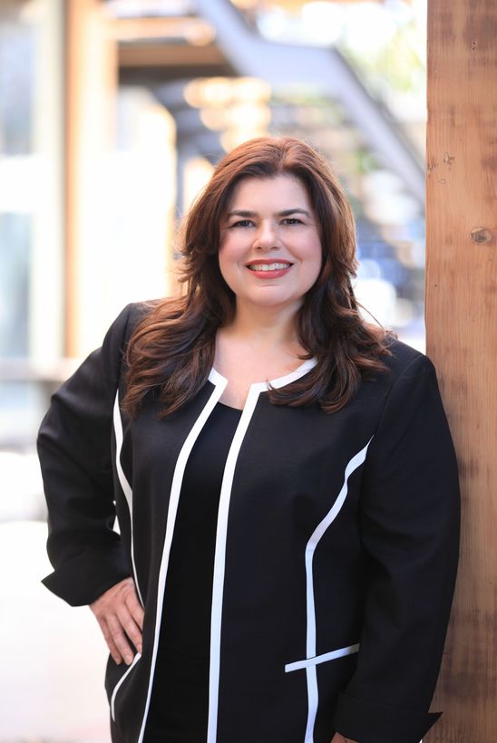 Lori Sinclair smiles at the camera while gently leaning against a wood post at The Cove on Bainbridge Island.