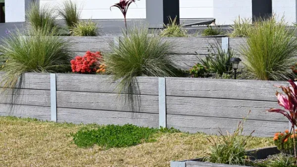 Stone retaining wall with grassy plants and colorful flowers — Chief Structural Landscaping In Glenvale, QLD