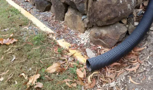 Black corrugated drainpipe near rocks and grass — Chief Structural Landscaping In Gold Coast, QLD