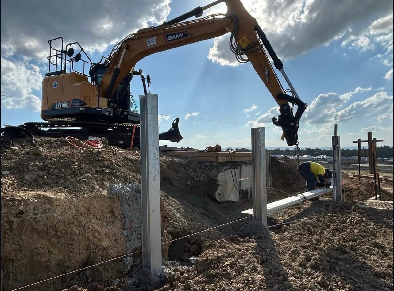An Excavator Placing Metal Fence Posts on a Construction Site — Chief Structural Landscaping In Glenvale, QLD