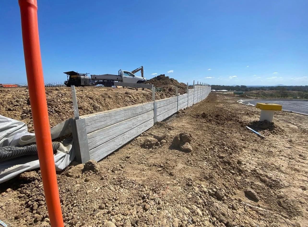 Concrete Retaining Wall, Dirt, Blue Sky, Excavator in Background — Chief Structural Landscaping In Glenvale, QLD