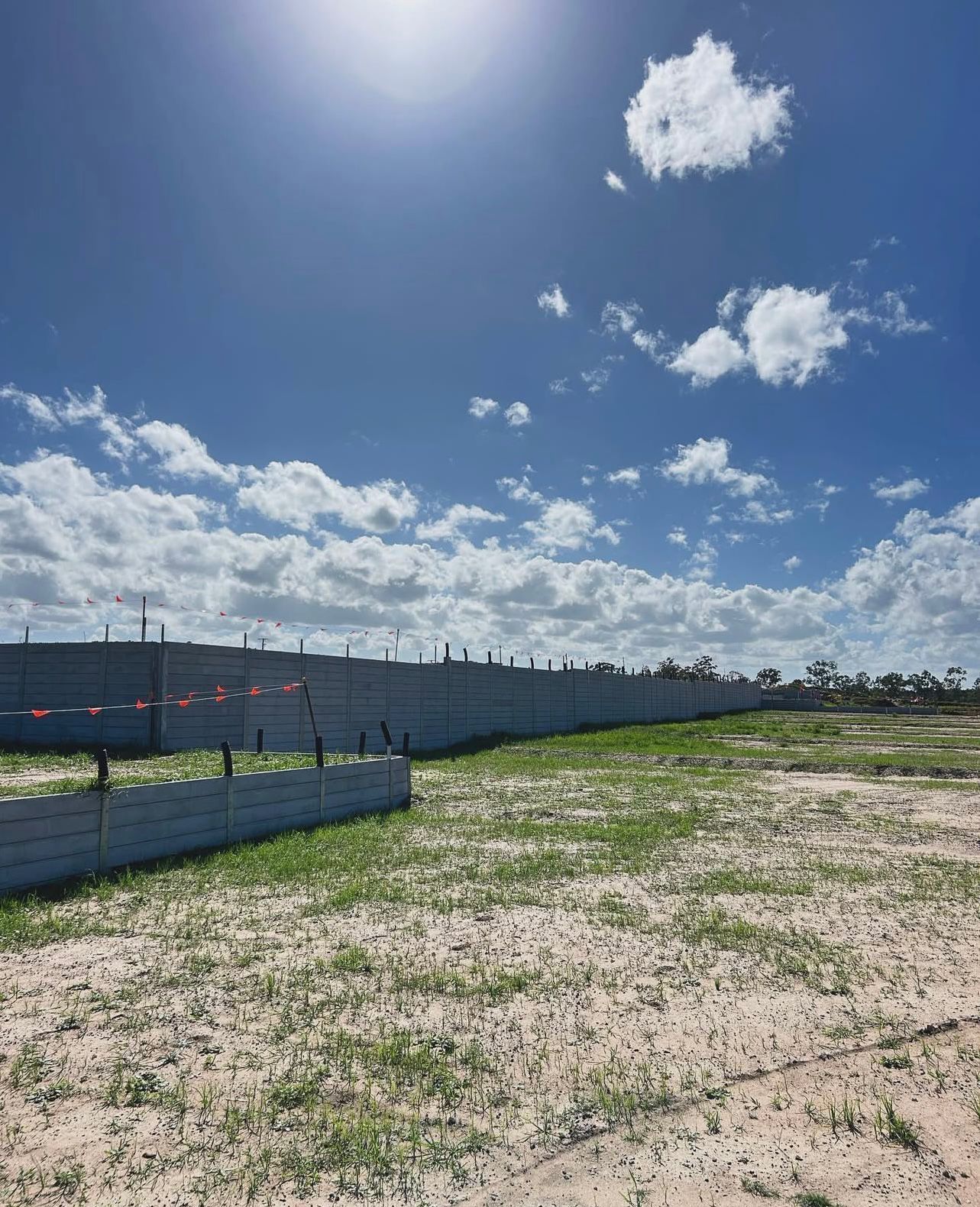Concrete Wall on a Grassy Lot Under a Bright Blue Sky With Fluffy Clouds — Chief Structural Landscaping In Glenvale, QLD